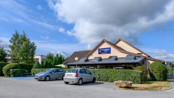 Restaurante de Comfort Hotel con aparcamiento, dos coches y un seto bien cuidado.
