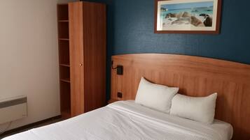 A hotel room with a wooden headboard, a white bedspread, a white pillow, a wooden wardrobe, and a framed picture on the wall.