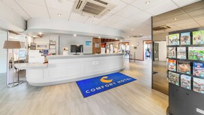 A reception area with a white counter, a blue carpet with the hotel logo, and a display of brochures. - Comfort Hotel Evreux (Evreux)
