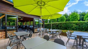 An outdoor patio area with tables and chairs, a large yellow umbrella, and a brick wall. - Comfort Hotel Evreux (Evreux)