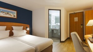 A hotel room with two beds, a wooden desk, a chair, and a bathroom visible through an open door. - Comfort Hotel Evreux (Evreux)