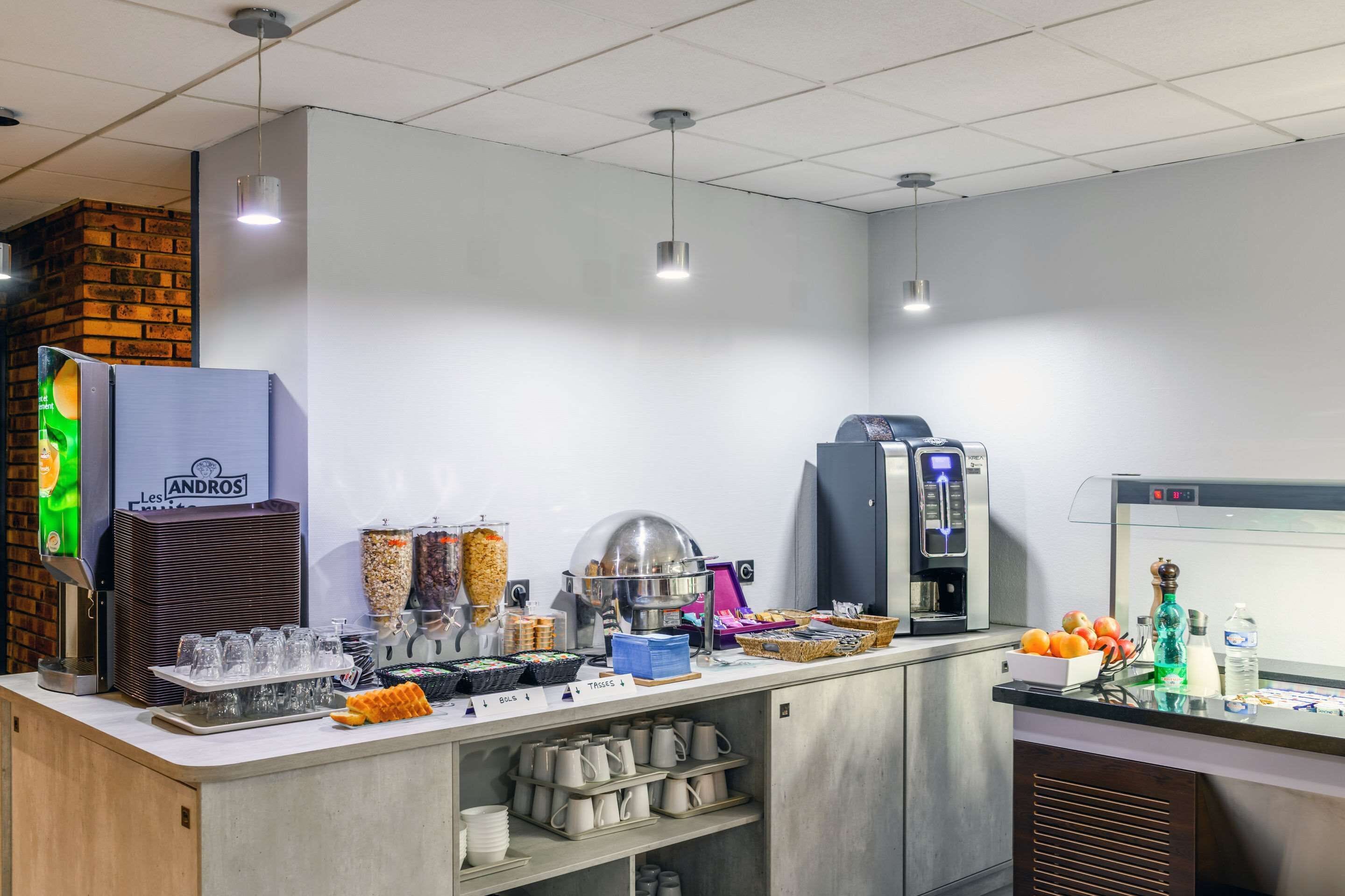 Un angolo colazione self-service con diversi distributori di cibo e bevande, tra cui una macchina per il caffè, un distributore di succhi e una selezione di cereali.