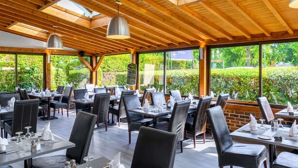 An outdoor dining area with wooden beams, tables set with white tableware, and a view of greenery. - Comfort Hotel Evreux (Evreux)