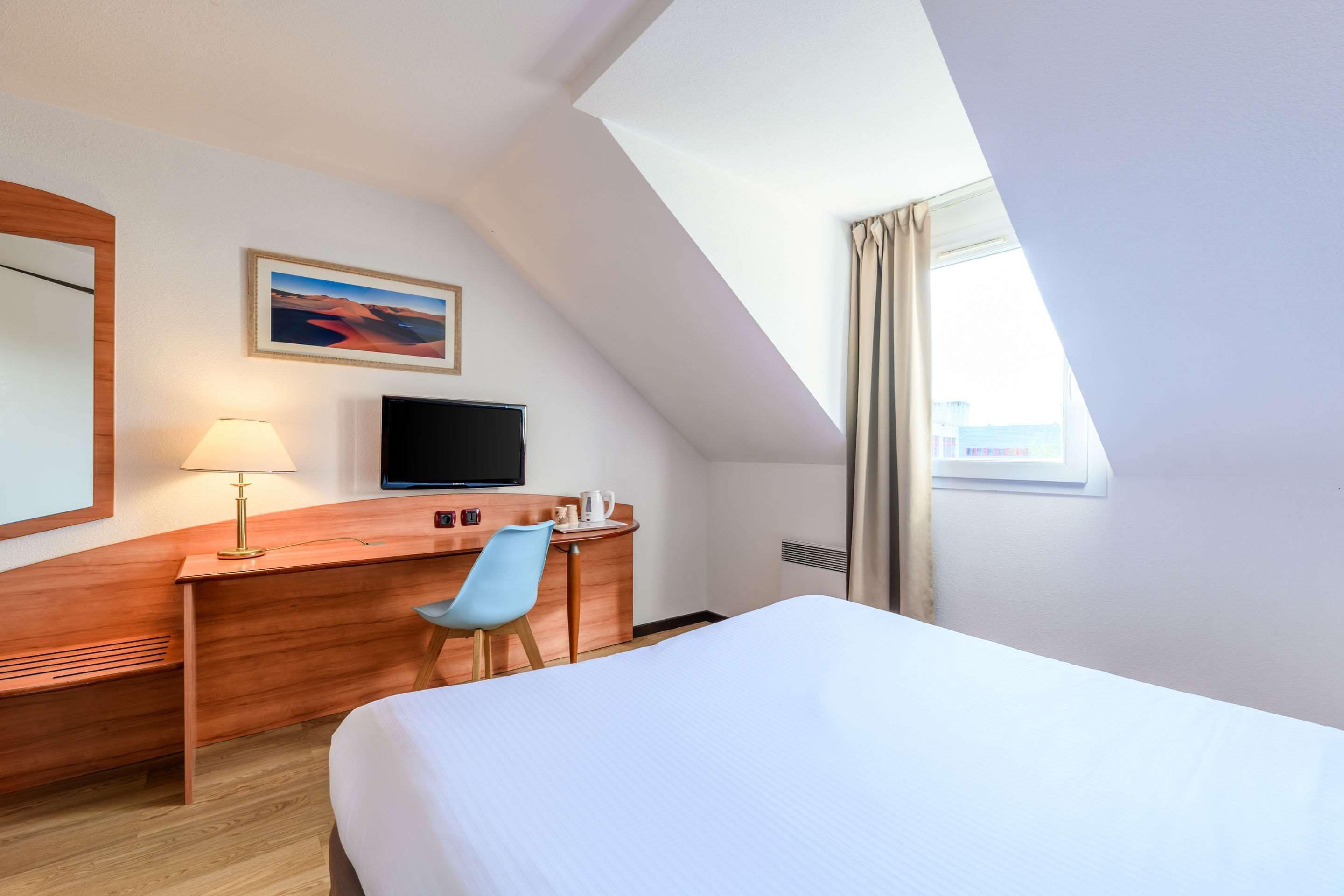 Une chambre d’hôtel avec un lit, un bureau et une chaise, une télévision, une lampe et un tableau au mur.