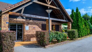 A brick building with a sloped roof and wooden beams, a sign indicating a restaurant, and a well-maintained garden with shrubs and a lamppost. - Comfort Hotel Evreux (Evreux)