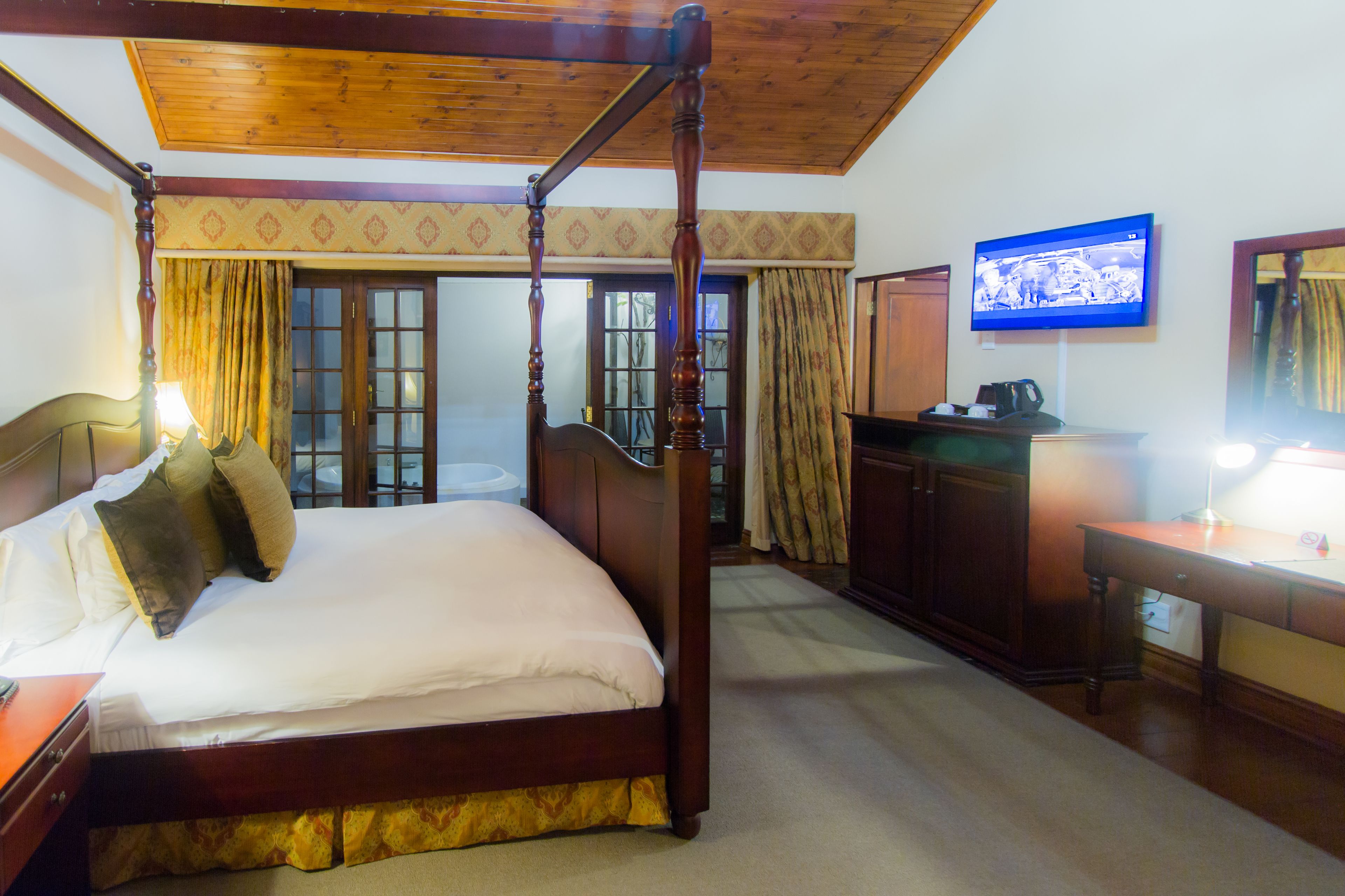 Una cama con dosel y tablero de madera, un escritorio con lámpara, y un televisor en la pared.