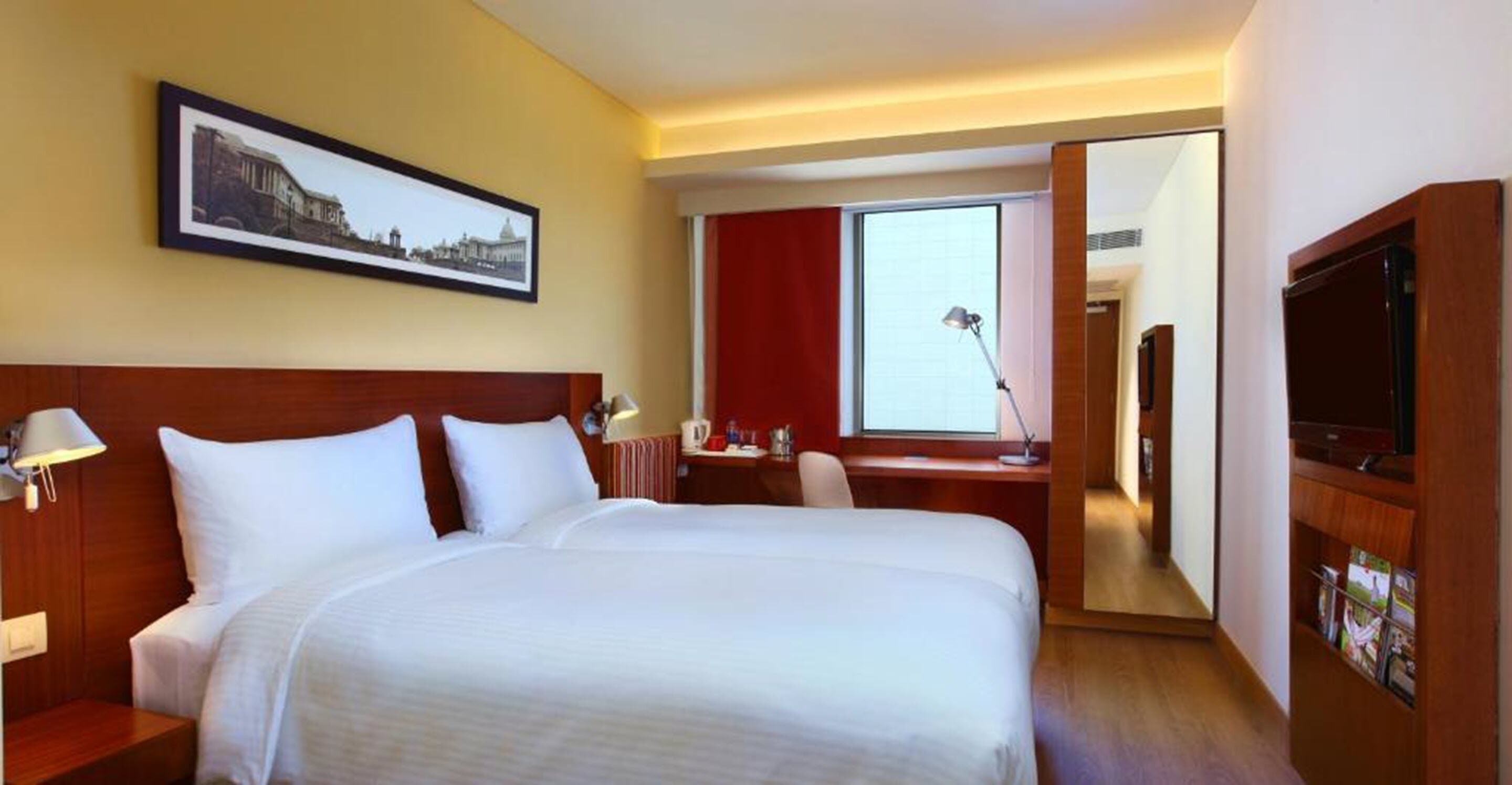 Ein Hotelzimmer mit einem großen Bett, einem Schreibtisch, einem Sessel, einem Fernseher und einem gerahmten Bild an der Wand.