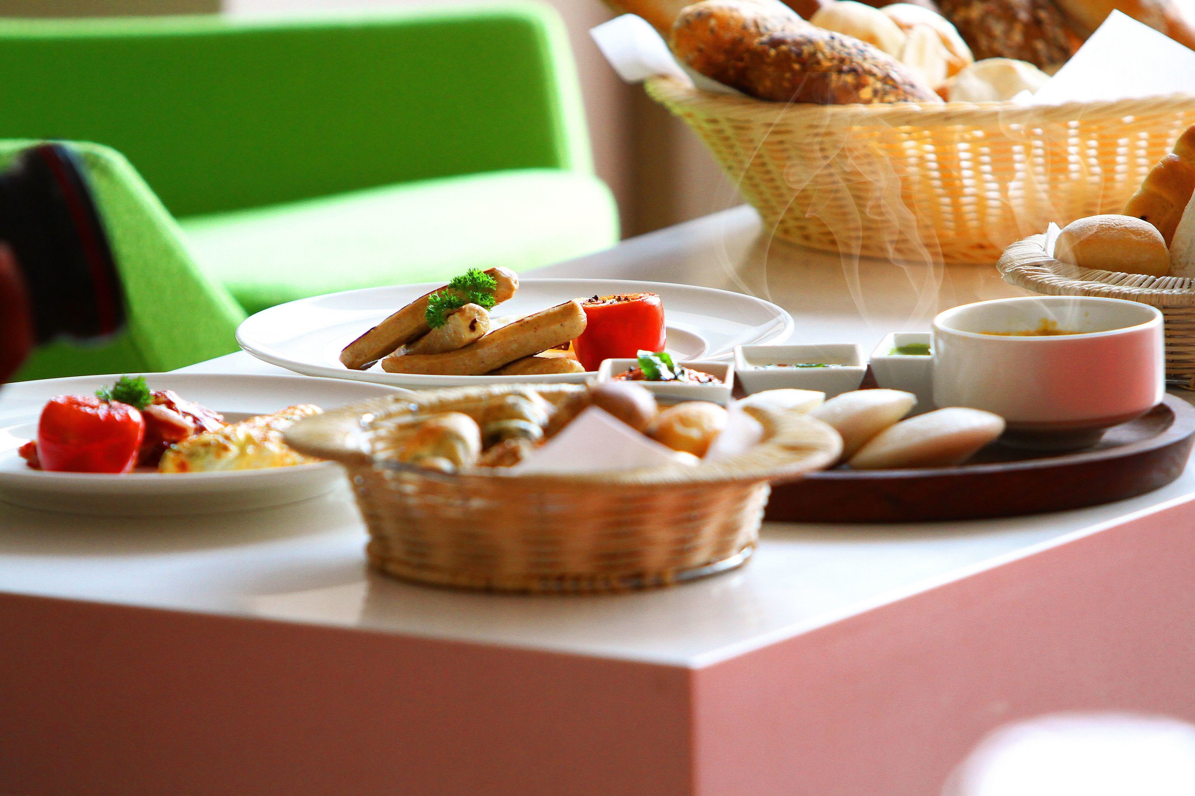 A breakfast setting with various food items on a table, including bread, pastries, and a plate with tomatoes and herbs.