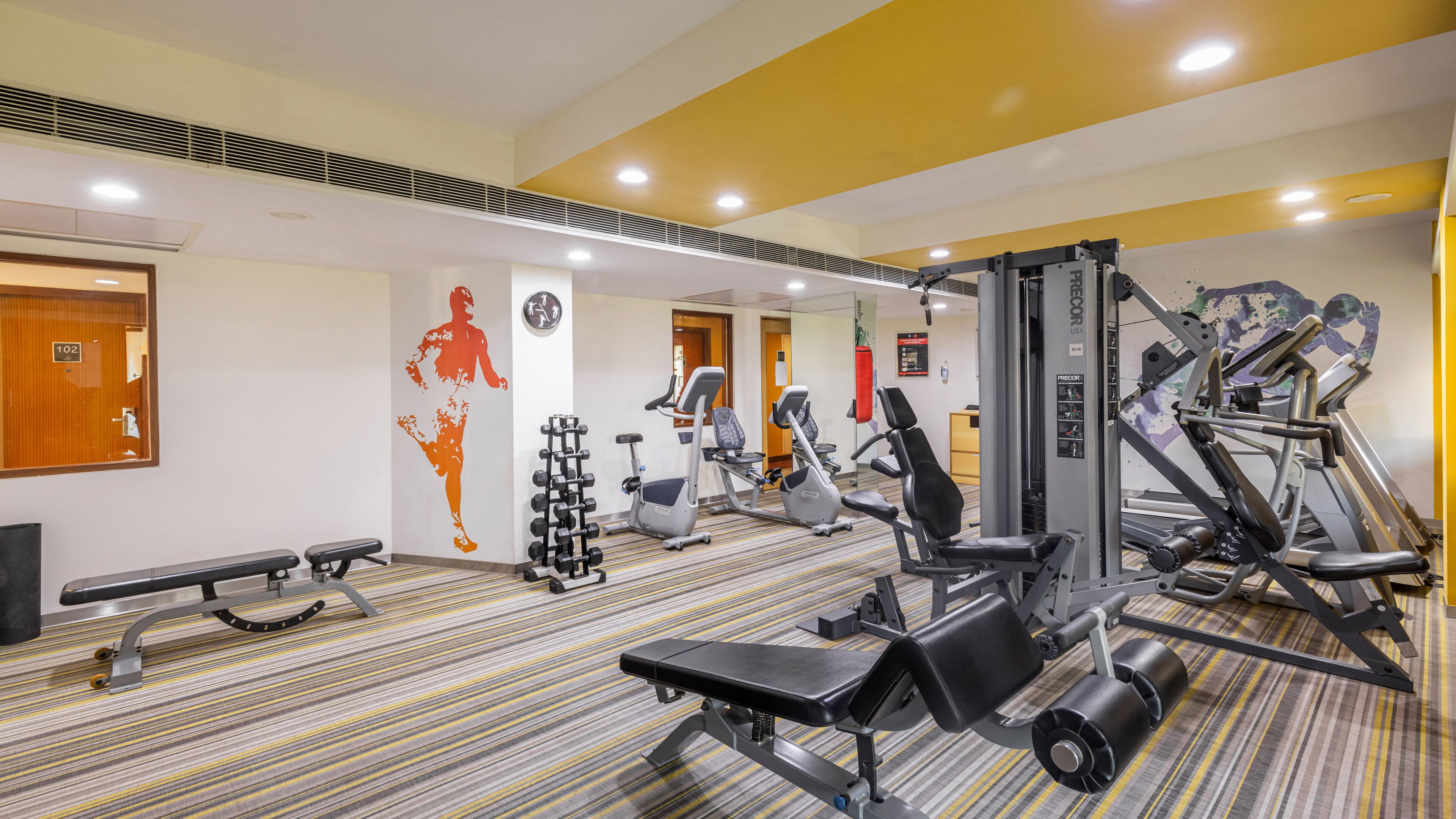 A gym with exercise equipment, a bench, and a wall with a silhouette.