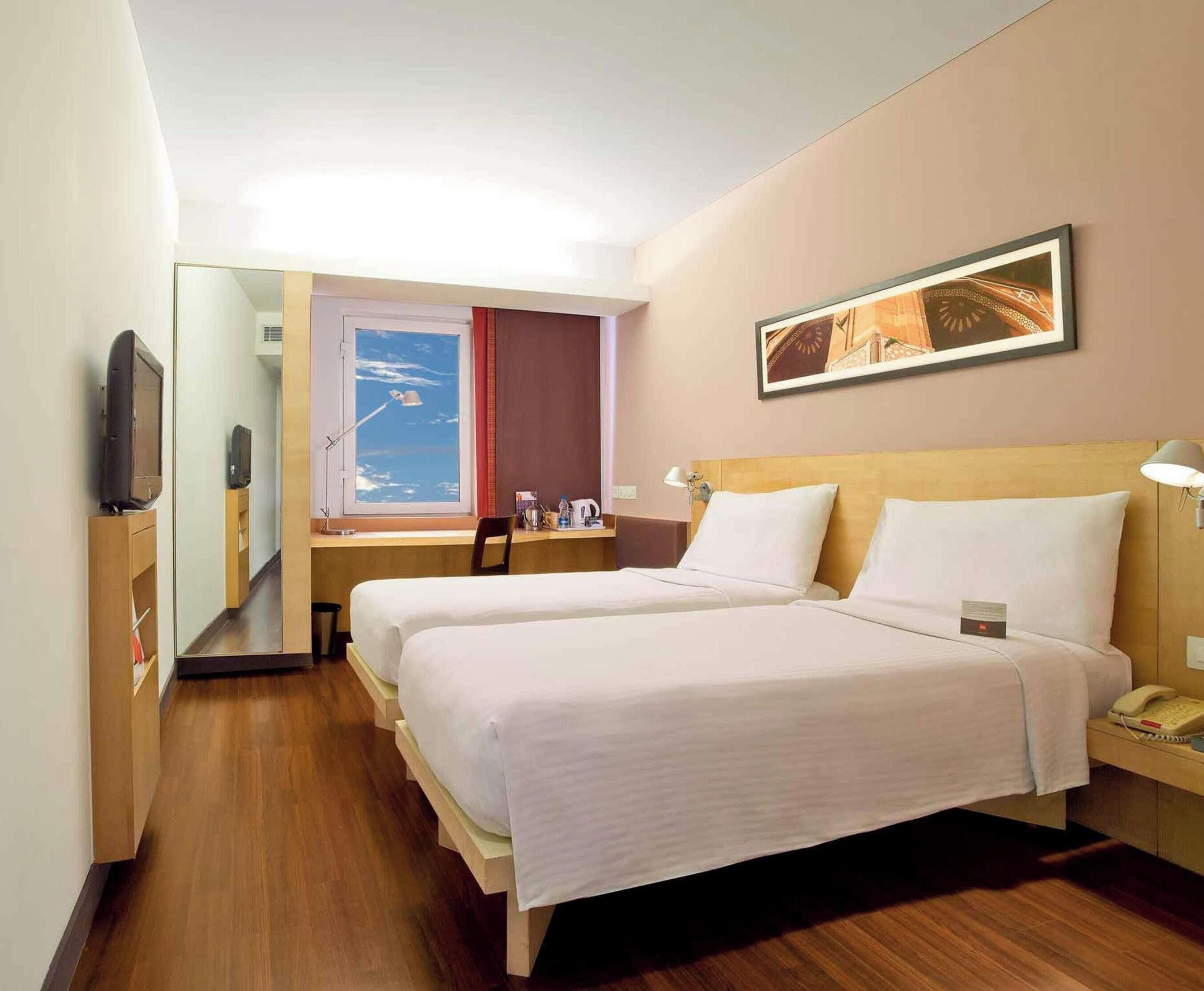 A hotel room with two beds, a desk, a chair, a TV, a window with a view, and a framed picture on the wall.