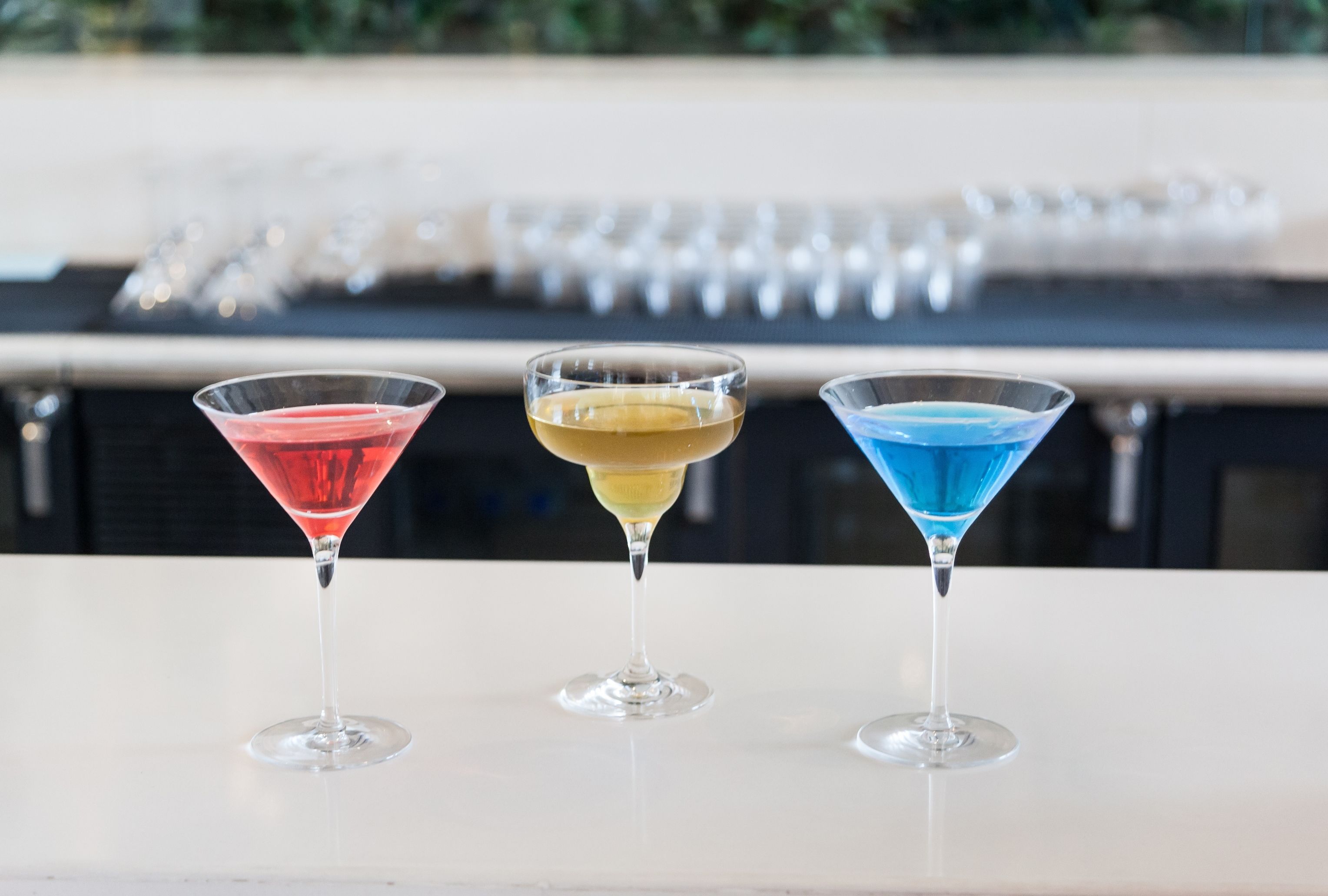 Three martini glasses with different colored drinks on a white surface.