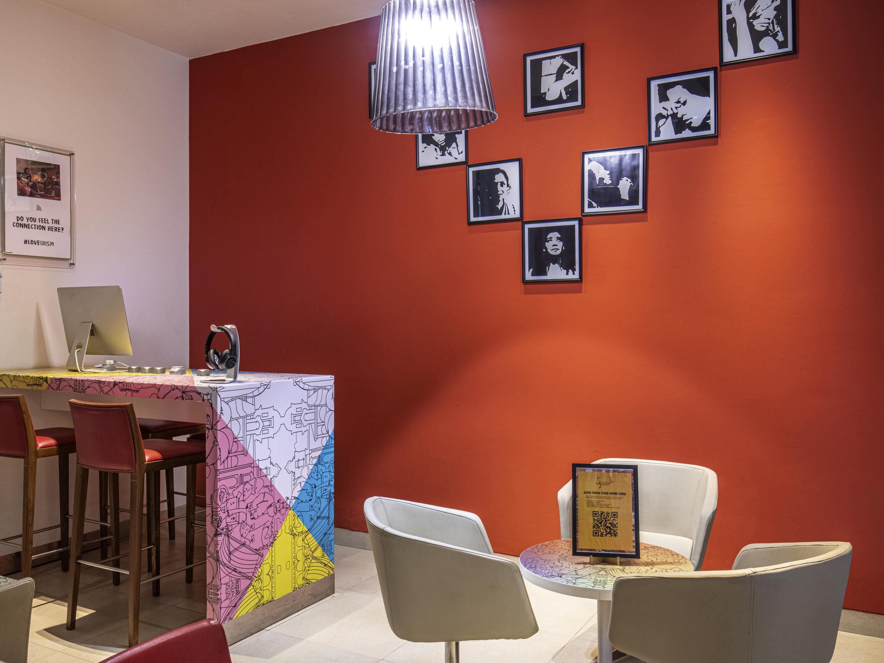 A room with a red wall, a desk with a computer, chairs, and framed pictures.
