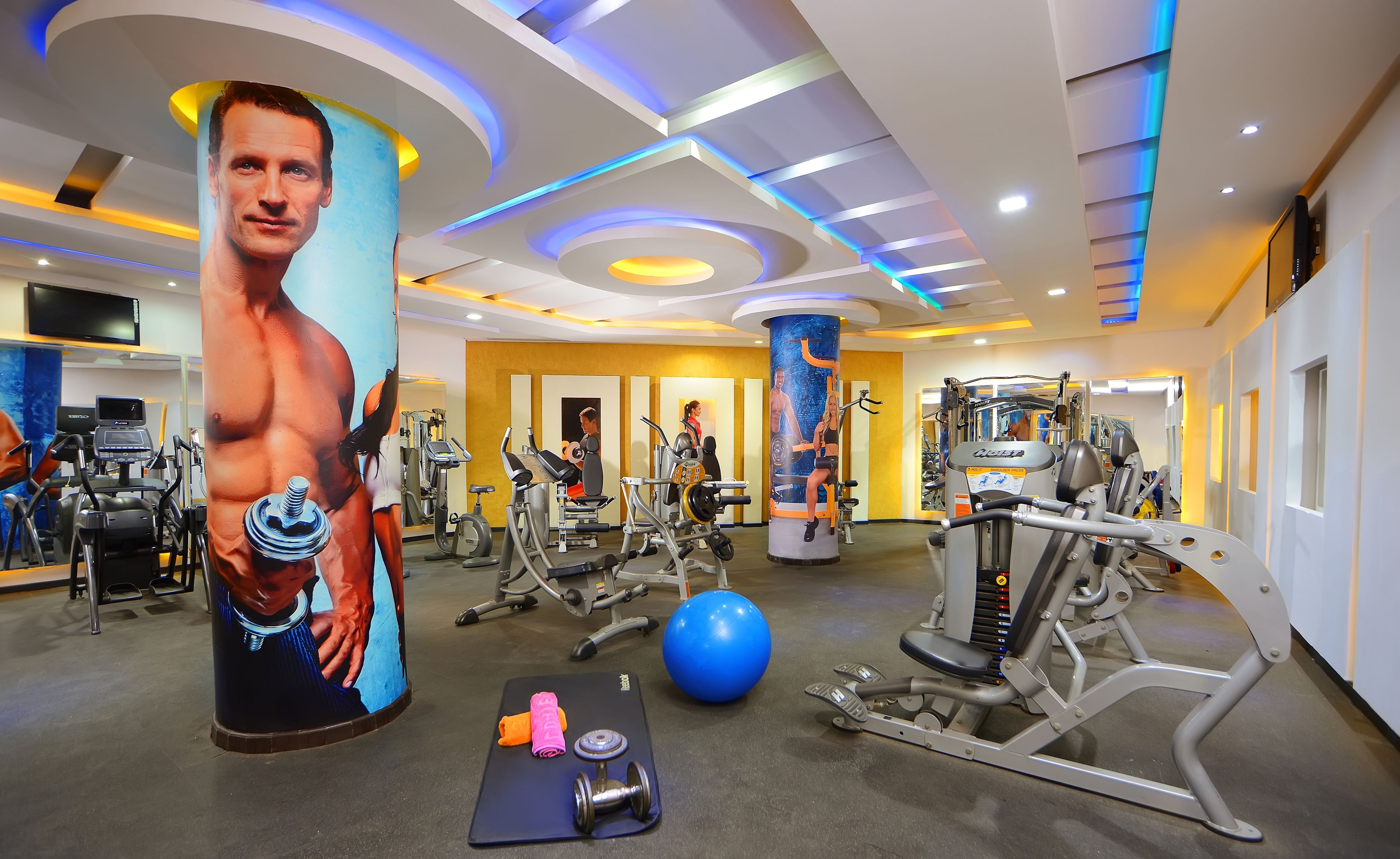 A gym with exercise equipment, a large poster, and a blue exercise ball.