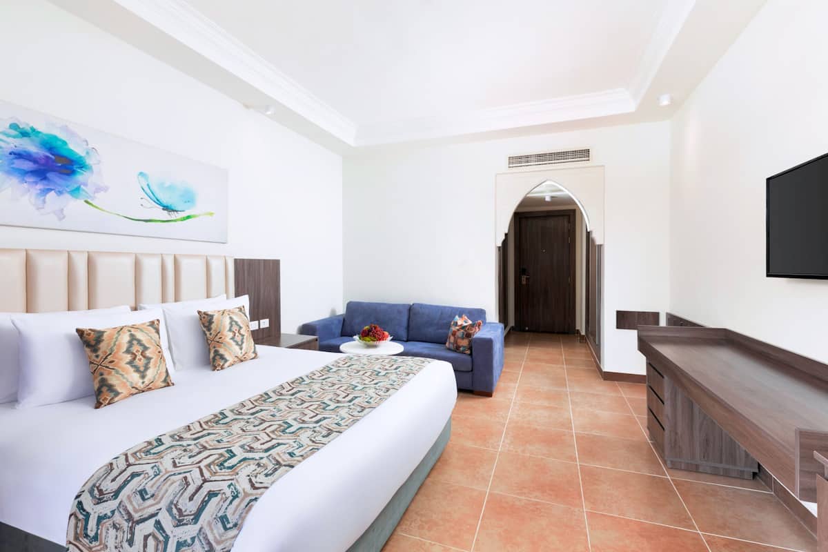 A hotel room with a large bed, a sofa, a TV, and a painting on the wall.