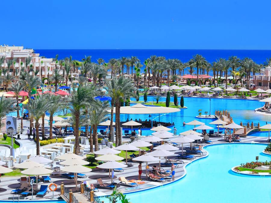 A resort with multiple swimming pools, palm trees, and beach umbrellas.