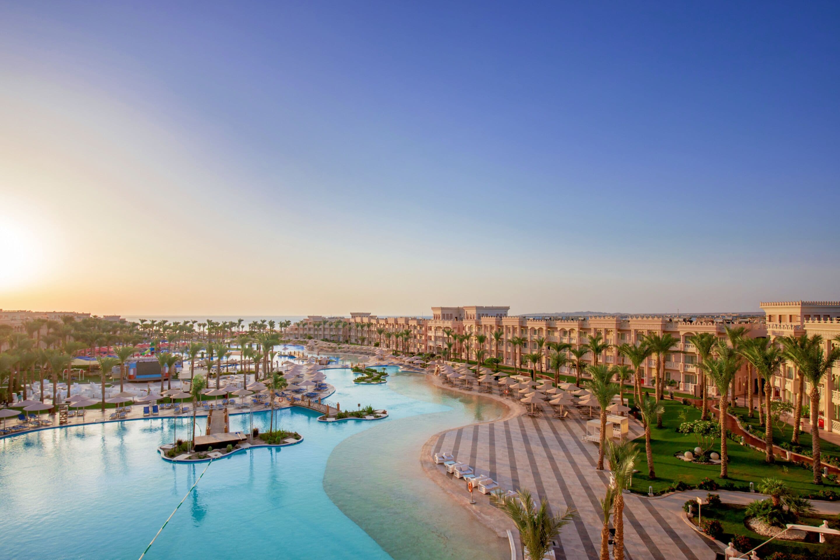 A resort with a large pool, palm trees, and a clear sky.