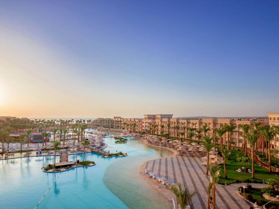A resort with a large pool, palm trees, and a clear sky.