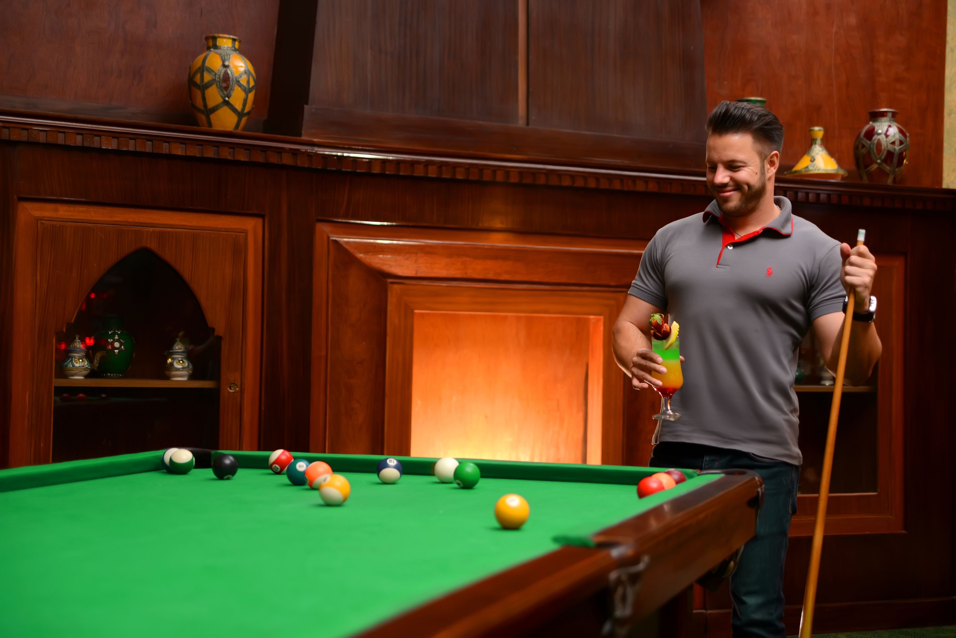 A pool table with balls, a cue stick, and decorative vases on shelves.