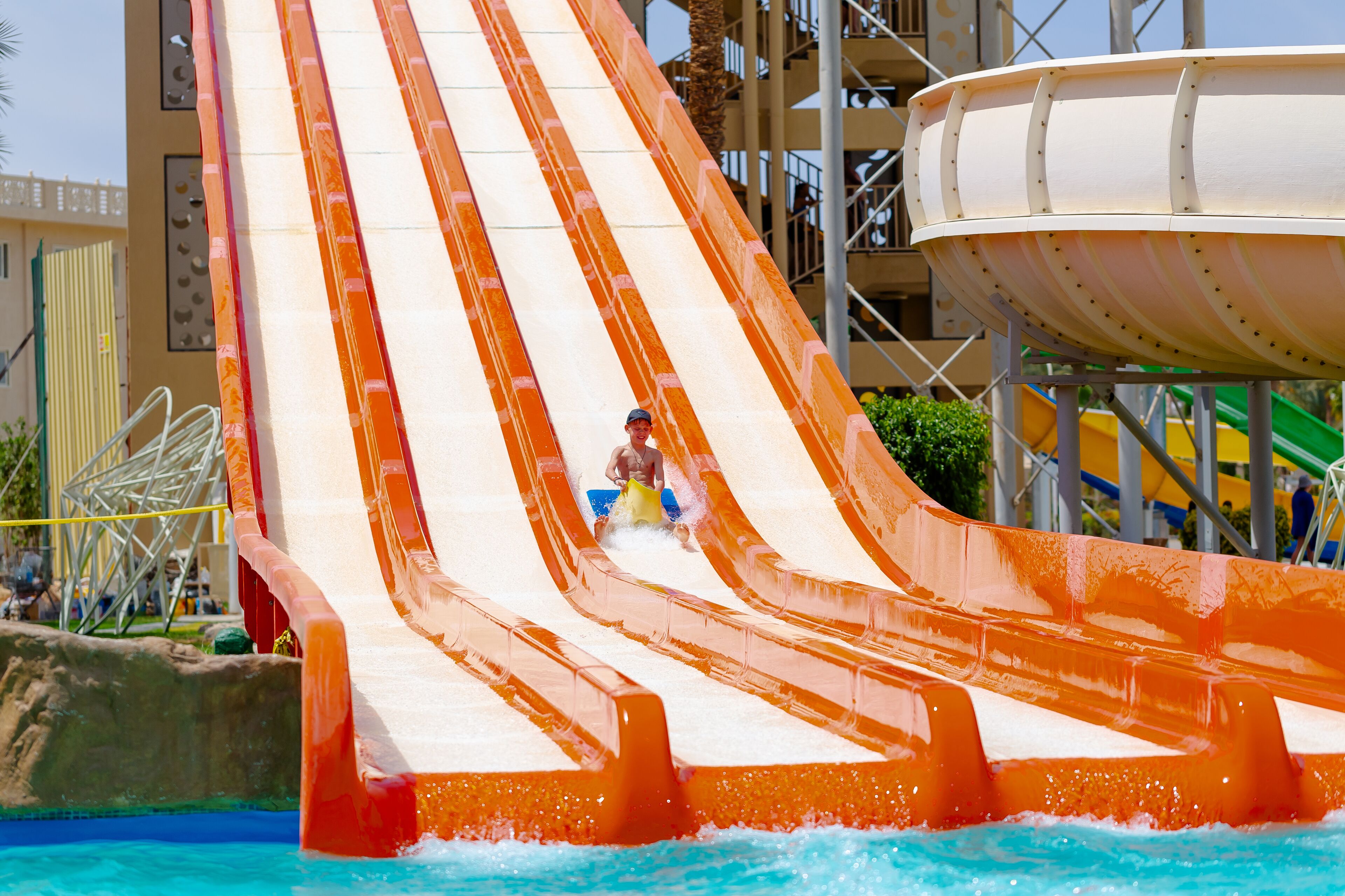 A water slide with multiple lanes, a pool at the bottom, and a building in the background.