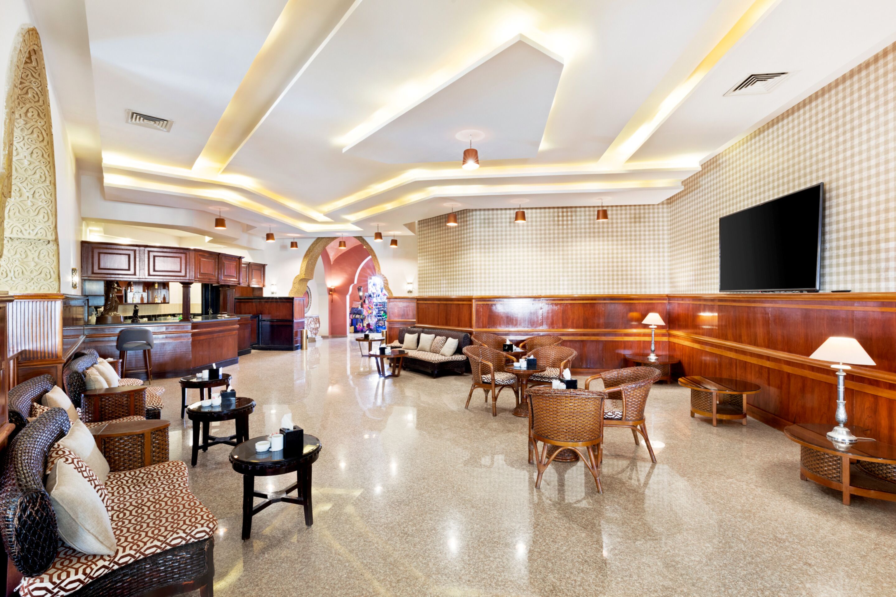 A spacious lobby with a modern design, featuring a seating area with sofas and chairs, a reception desk, and a large flat-screen TV on the wall.