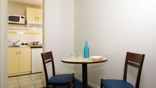 A small dining area with two chairs, a table, a microwave, and a sink in the background. - Appart'City Classic Clermont Ferrand Centre (Clermont-Ferrand)