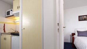 A compact hotel room with a kitchenette, a bed with white bedding, and a small bedside table. - Appart'City Classic Clermont Ferrand Centre (Clermont-Ferrand)