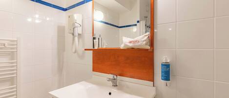 A bathroom with a white sink, a mirror, a towel dispenser, and a hand dryer.