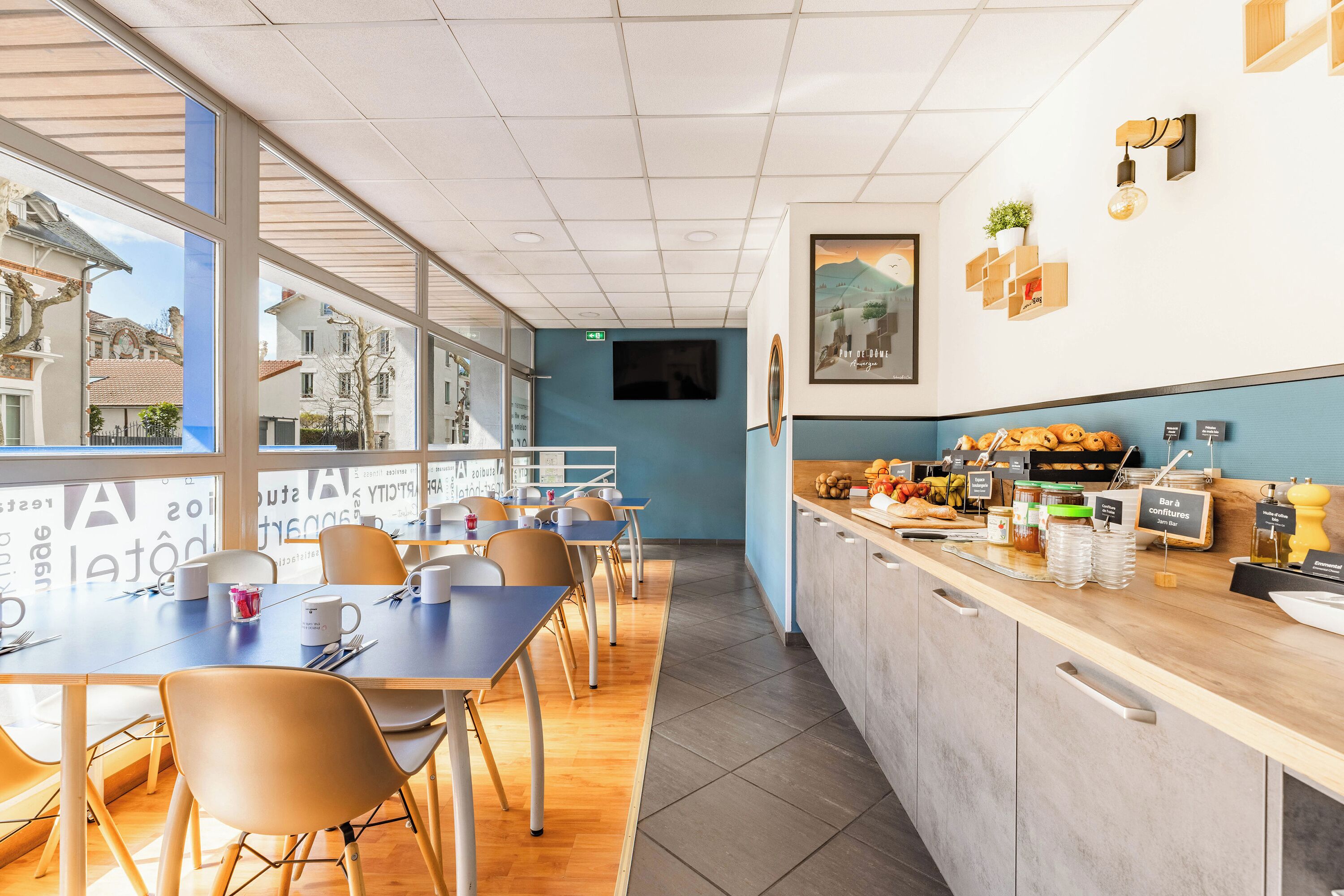 Een modern café met een lange balie, een zithoek en grote ramen.