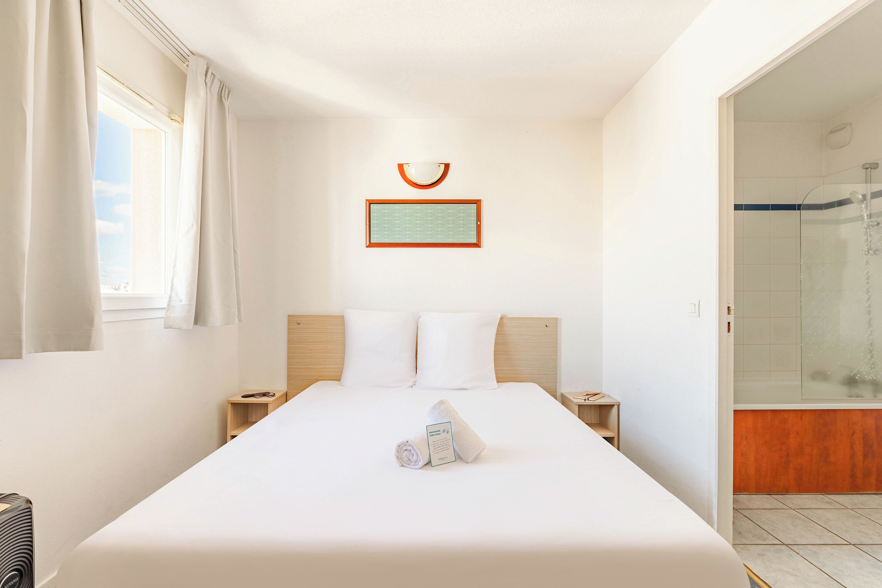 Una camera d'albergo con un letto grande, un comodino, una lampada da comodino, un quadro incorniciato e un angolo doccia.