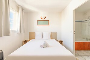 A hotel room with a large bed, a bedside table, a nightstand, a framed picture, and a shower area.