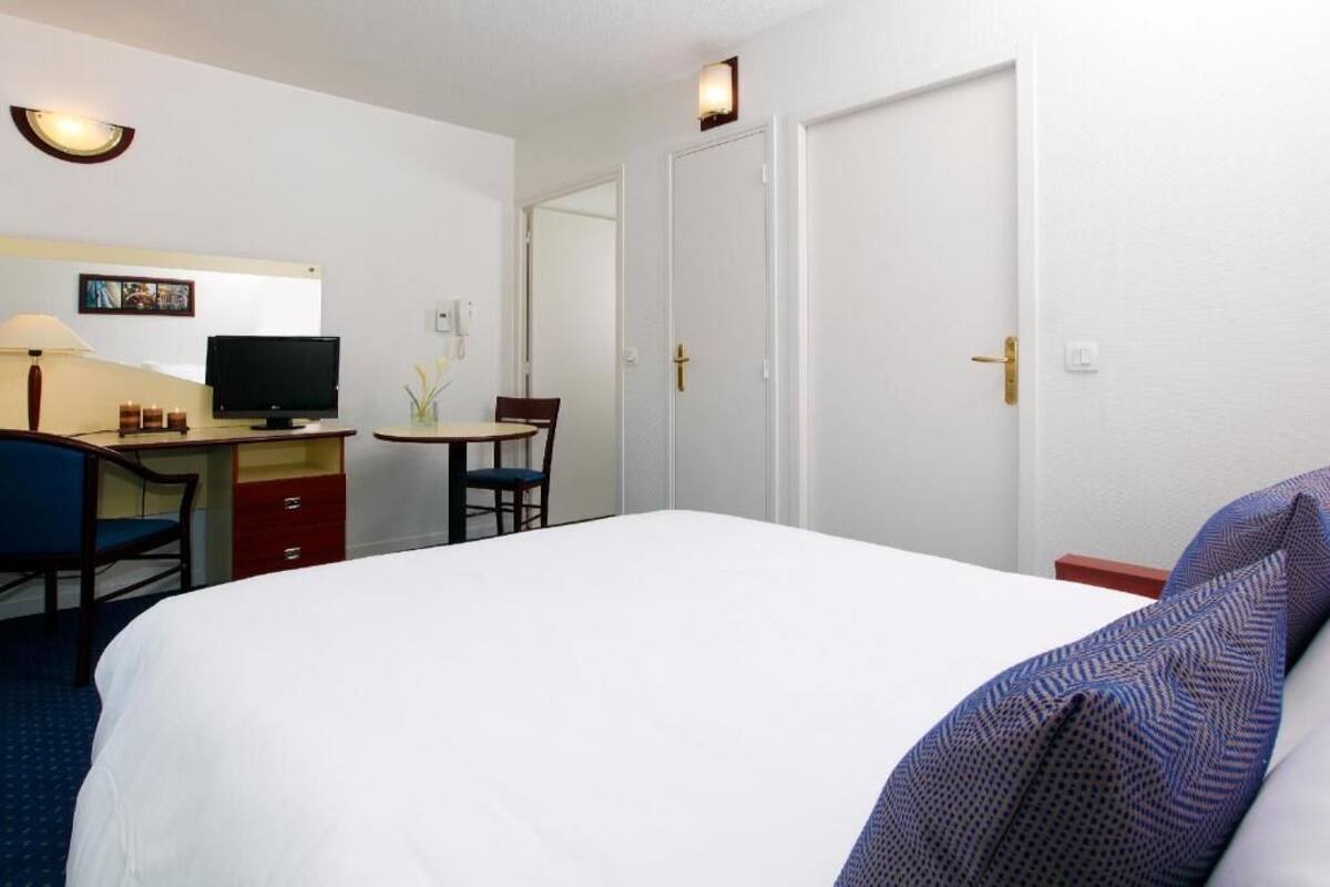 Una habitación de hotel con cama, escritorio con computadora, silla y televisor.
