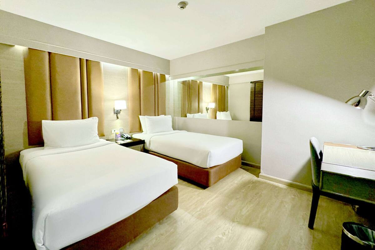 Una habitación de hotel con dos camas, un escritorio, una silla y un espejo grande.