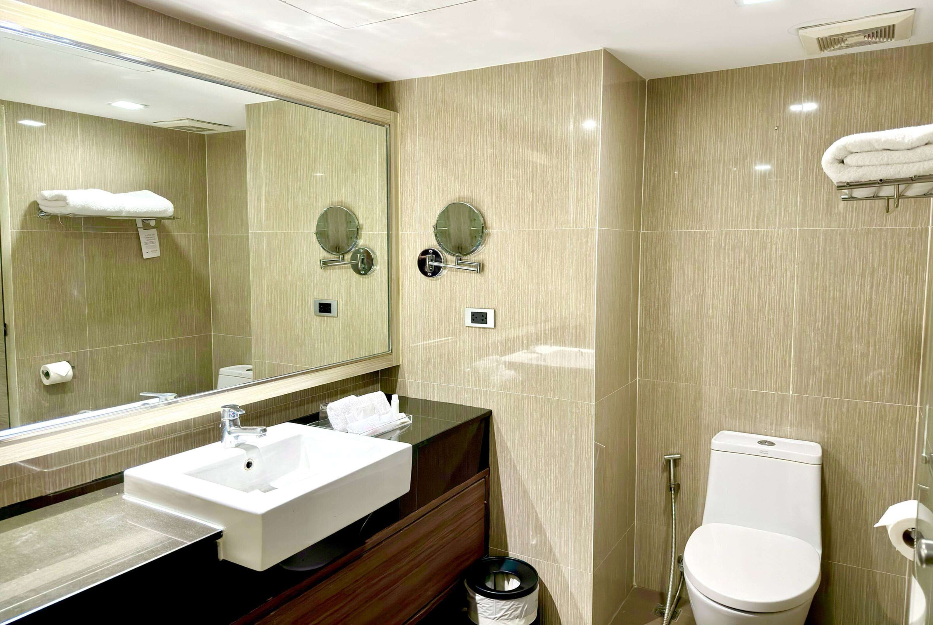 A modern bathroom with a sink, mirror, toilet, and towel rack.