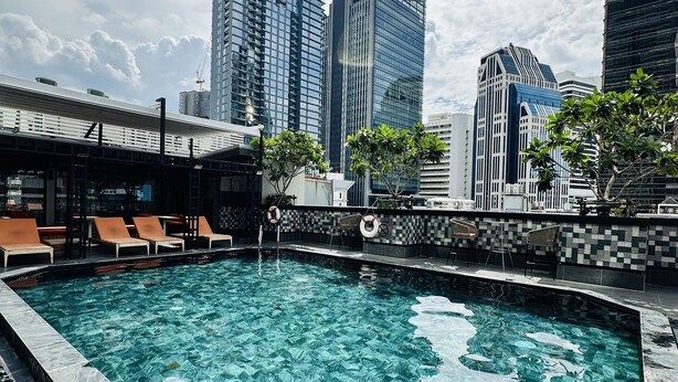 Une piscine avec vue sur le paysage urbain, entourée de chaises longues et d’une terrasse carrelée.