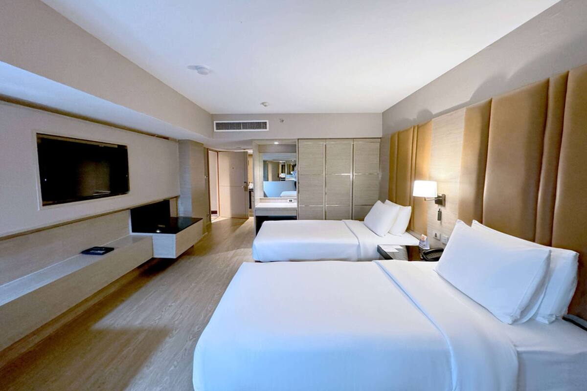 Habitación de hotel con dos camas, televisor montado en la pared, mesita de noche y armario.