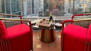 Un balcon avec des chaises rouges, une table garnie de nourriture et de boissons, et une vue sur la ville.