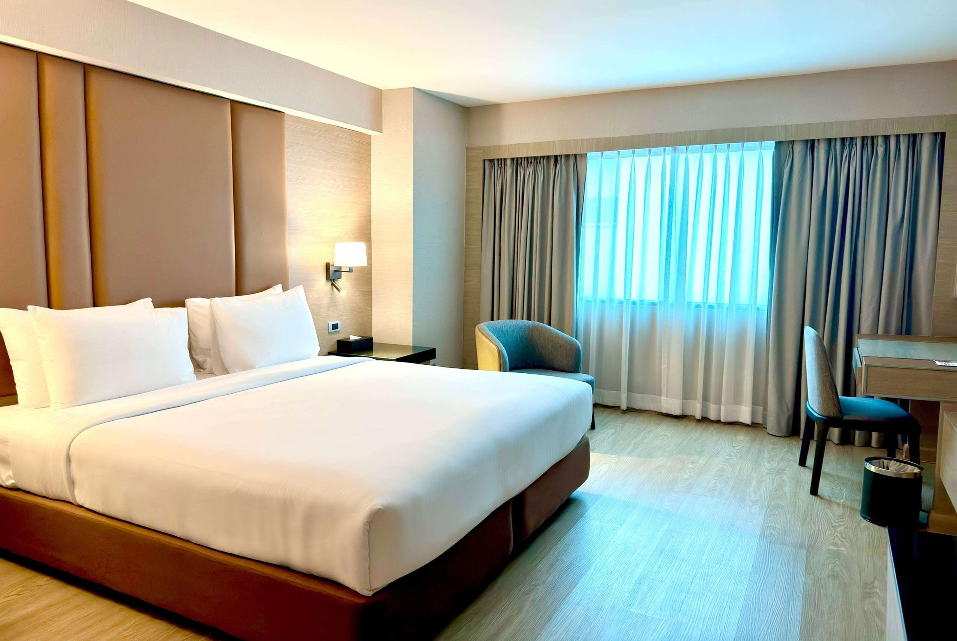 Habitación de hotel con una cama grande, un escritorio, una silla y un ventanal con cortinas.
