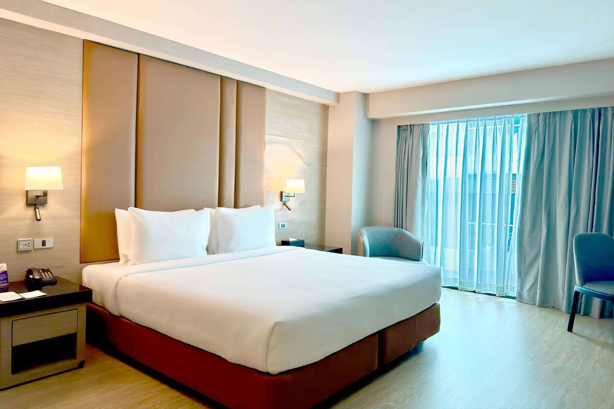 Una habitación de hotel con una cama grande, lámparas de noche, un escritorio con teléfono y una silla.