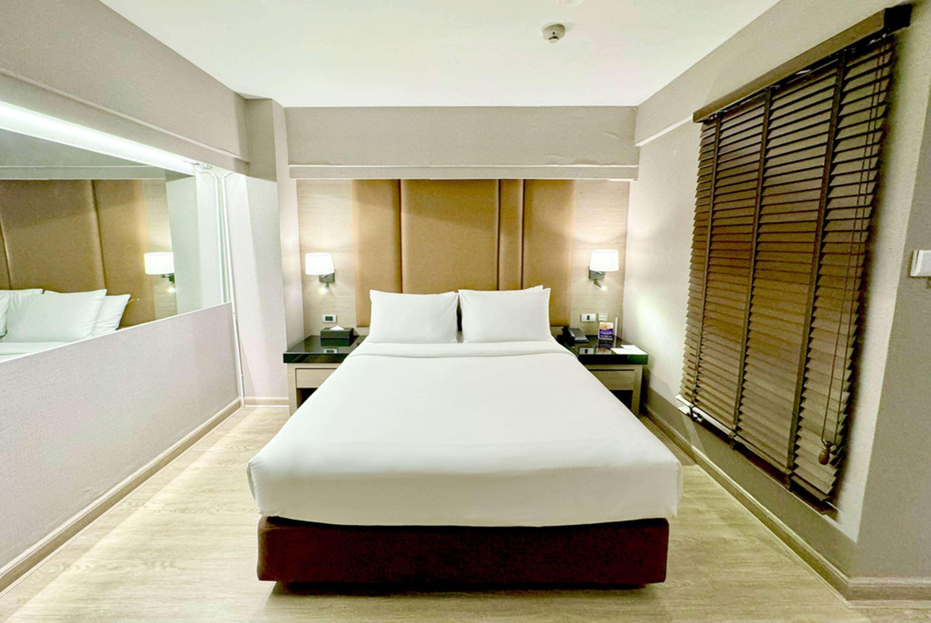 A hotel room with a large bed, bedside tables, a mirror, and a window with blinds.