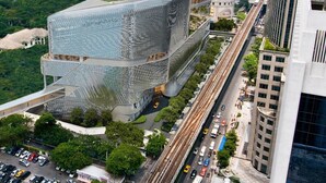 Un gratte-ciel moderne au design original et audacieux, entouré d’un paysage urbain et de verdure.