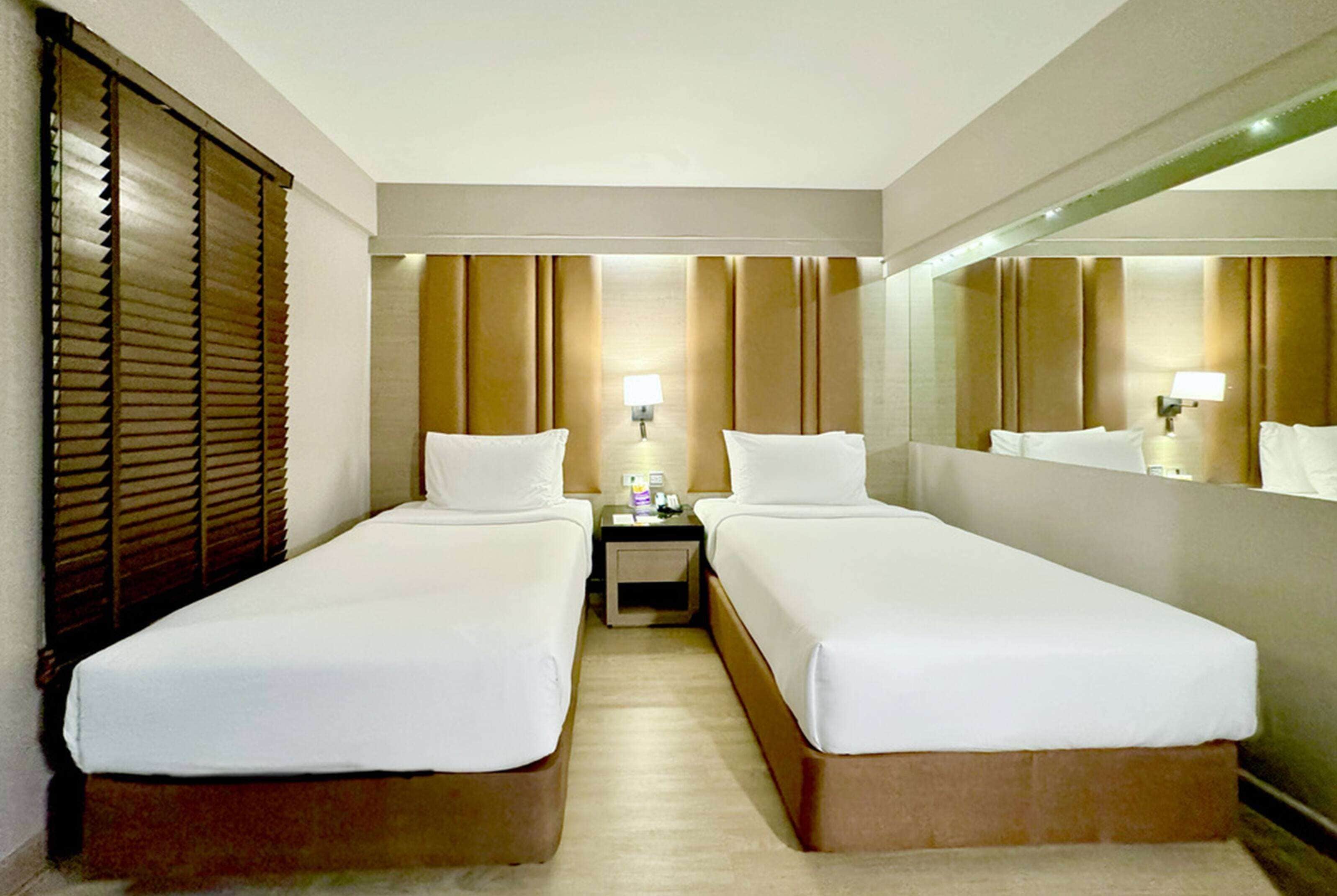 A hotel room with two single beds, a nightstand with a lamp, and a large mirror on the wall.