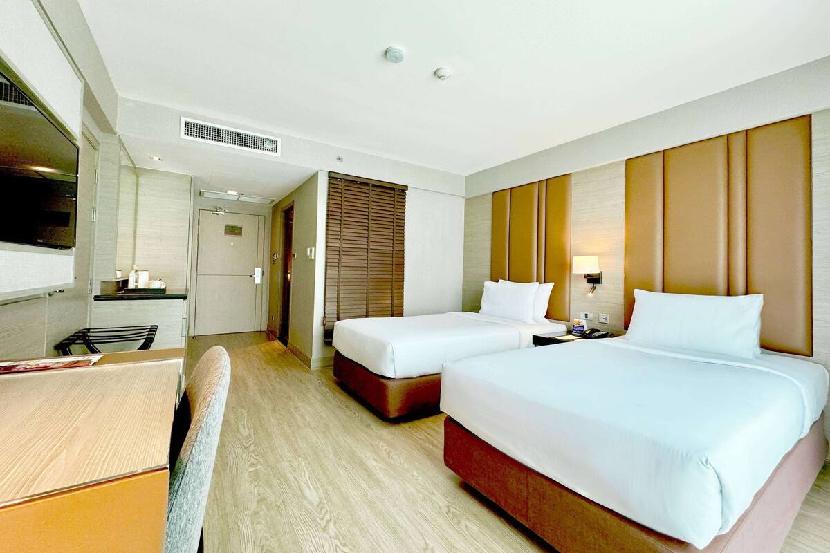 Habitación de hotel con dos camas, un escritorio, una silla, un televisor y un baño.