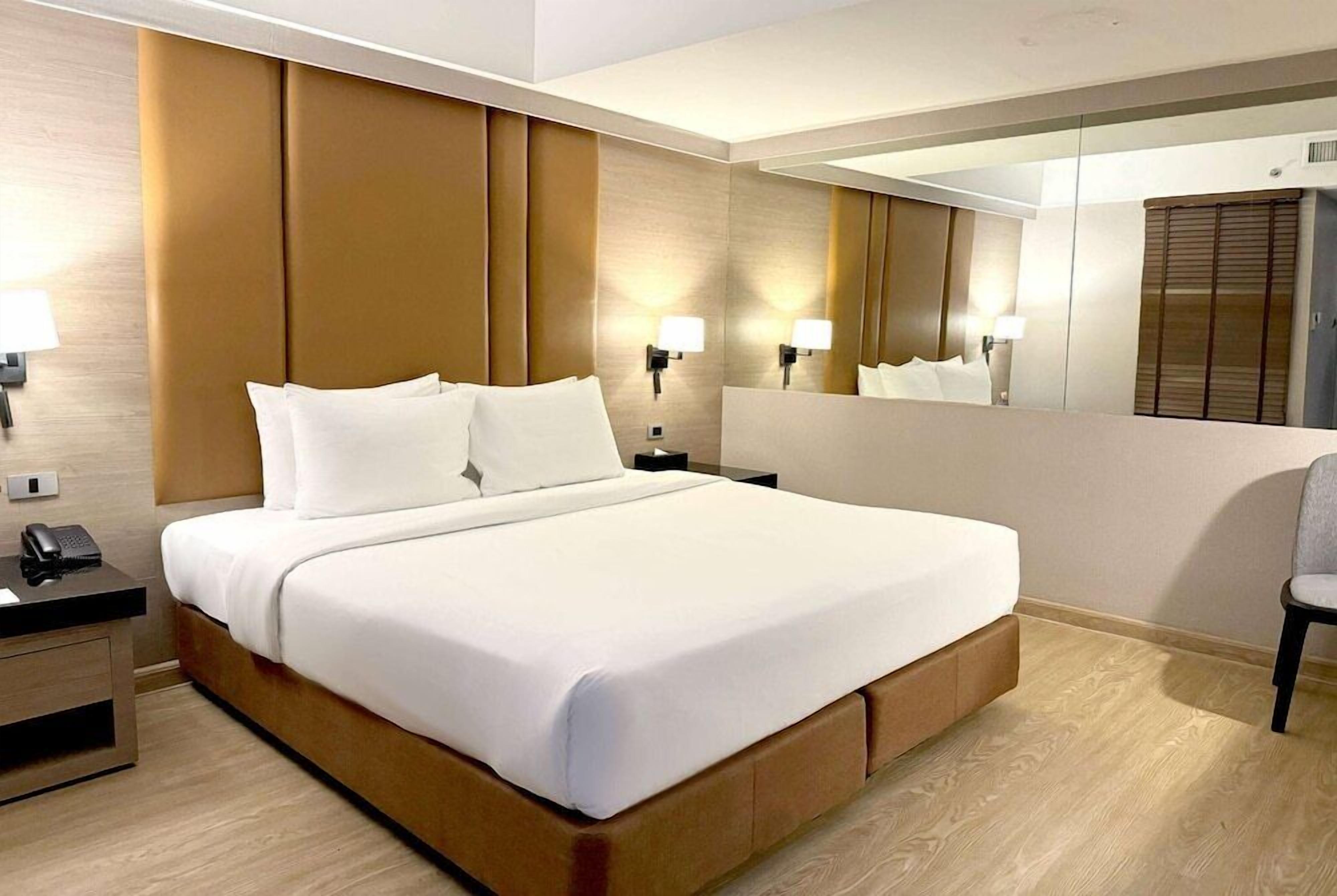A hotel room with a large bed, bedside lamps, a telephone, and a mirror.
