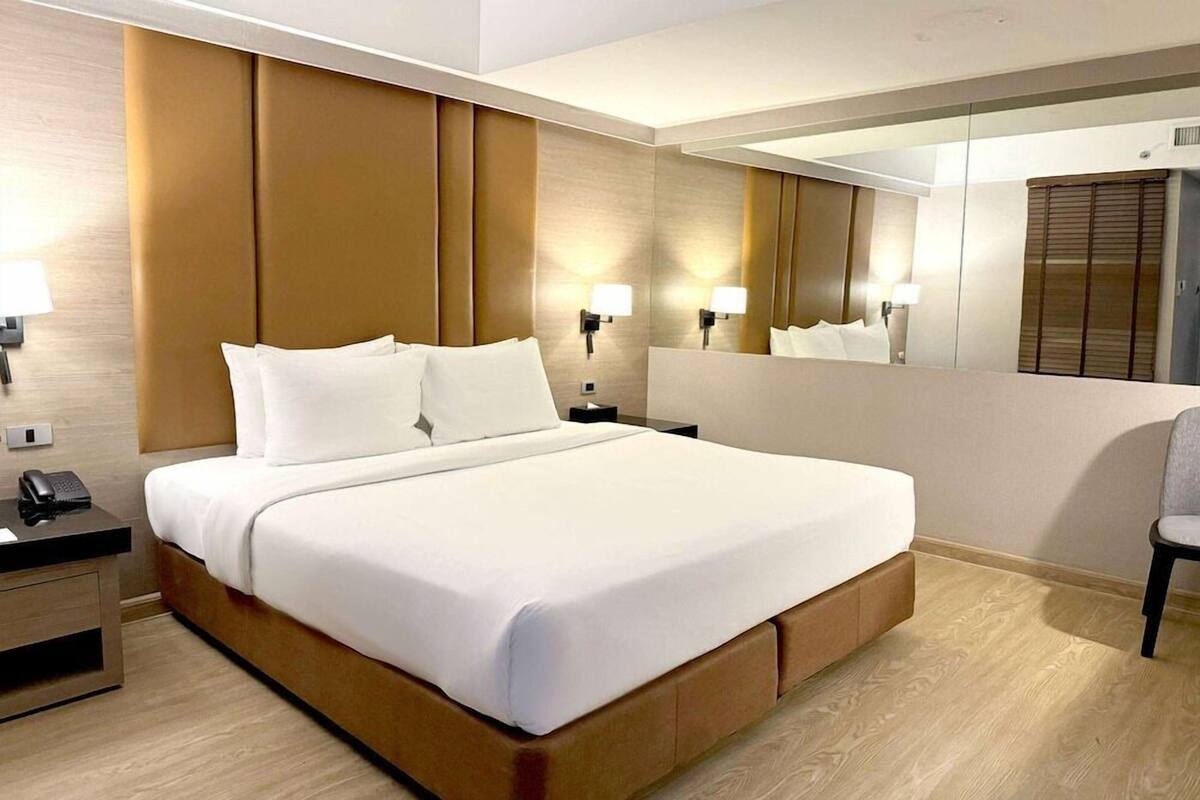 Habitación de hotel con una cama grande, lámparas de noche, un teléfono y un espejo.