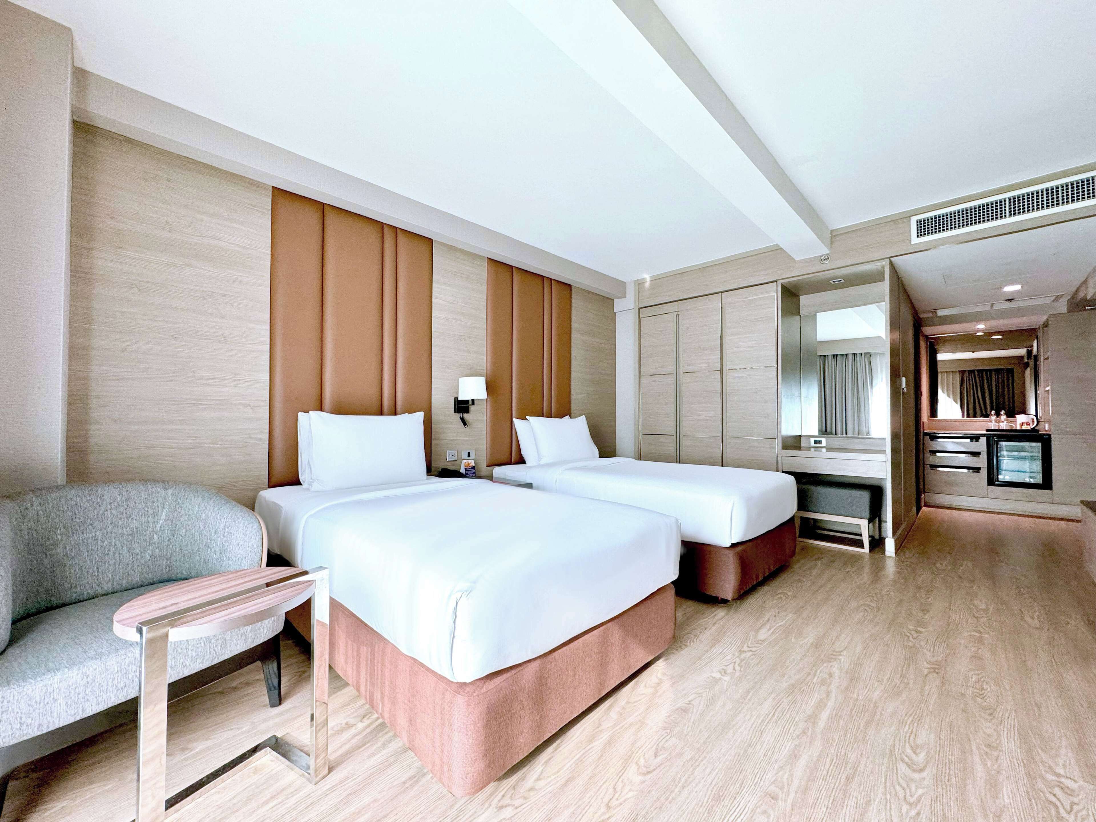 A hotel room with two beds, a sofa, a small table, a mirror, and a kitchenette.