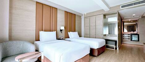 A hotel room with two beds, a sofa, a small table, a mirror, and a kitchenette.