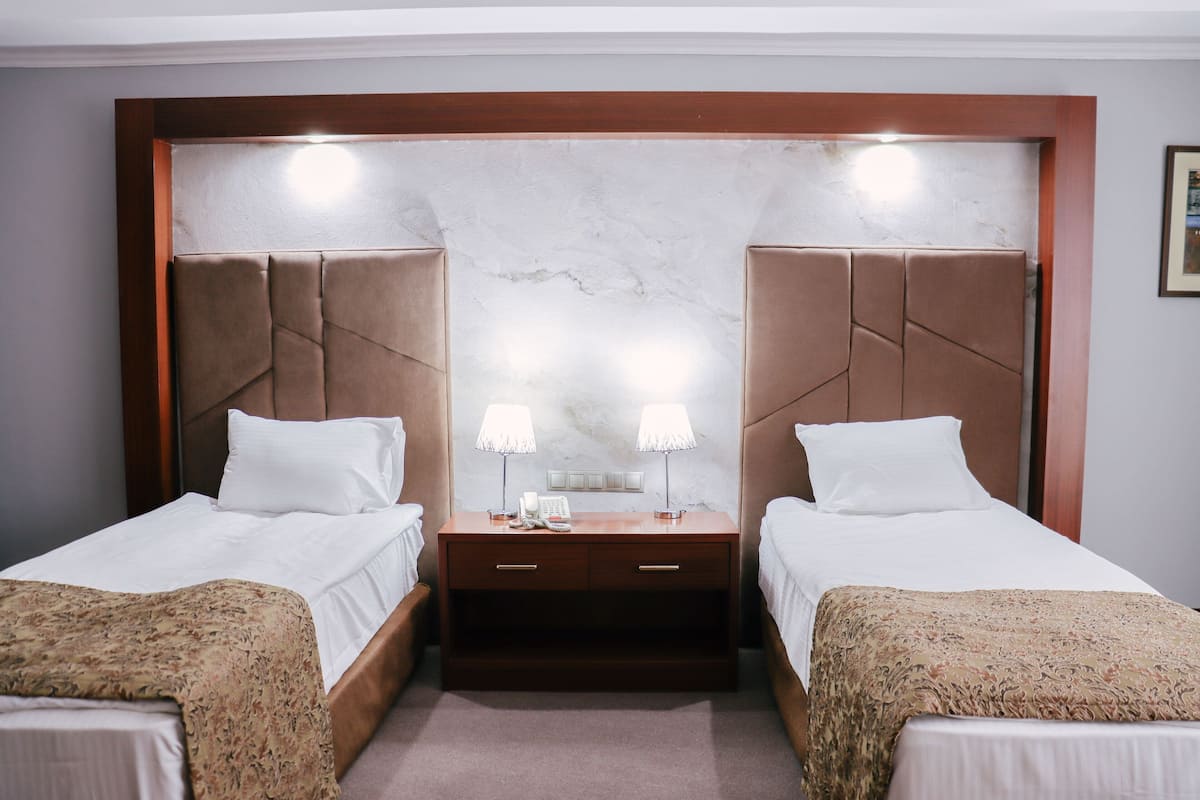 A hotel room with two beds, a nightstand with lamps, and a marble headboard.