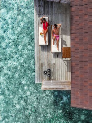 An aerial view of a wooden deck with two lounge chairs, a small table, and a brick wall. - Ellaidhoo Maldives by Cinnamon (Ellaidhoo)
