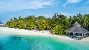A beach resort with a thatched-roof hut, white sandy beach, clear turquoise waters, and lush palm trees. - Ellaidhoo Maldives by Cinnamon (Ellaidhoo)