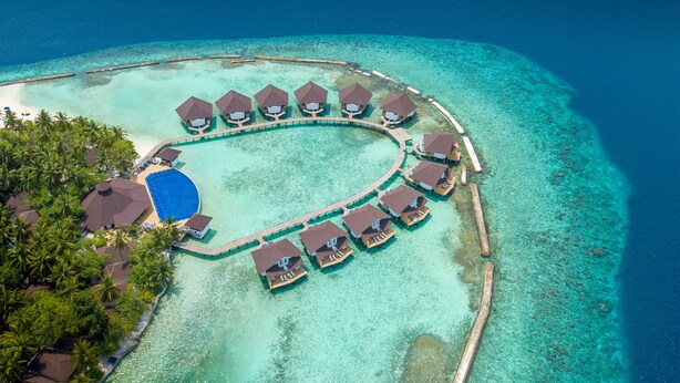 An aerial view of a resort with overwater bungalows arranged in a semi-circle around a central pool, connected by walkways. - Ellaidhoo Maldives by Cinnamon (Ellaidhoo)